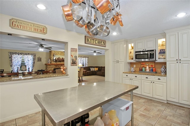 kitchen with glass insert cabinets, a healthy amount of sunlight, stainless steel microwave, and a textured ceiling