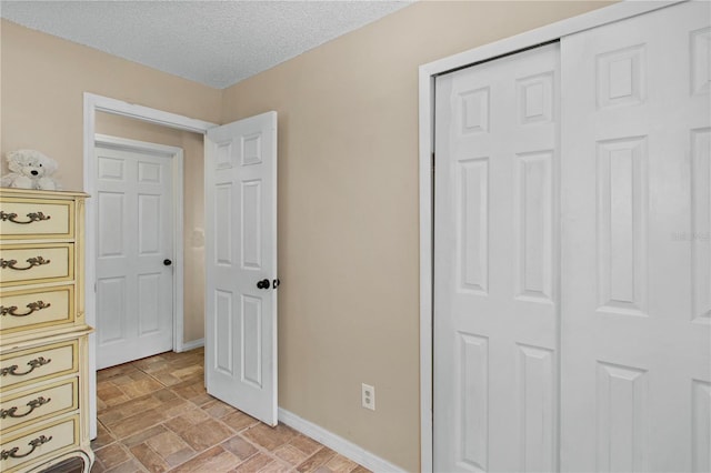 unfurnished bedroom featuring a textured ceiling, stone finish flooring, and baseboards