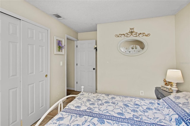 bedroom featuring baseboards, visible vents, a textured ceiling, and wood finished floors