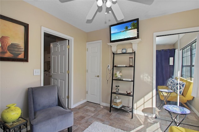 sitting room with a ceiling fan, stone finish flooring, a textured ceiling, and baseboards