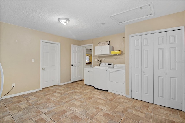 clothes washing area with attic access, baseboards, stone finish floor, independent washer and dryer, and a textured ceiling