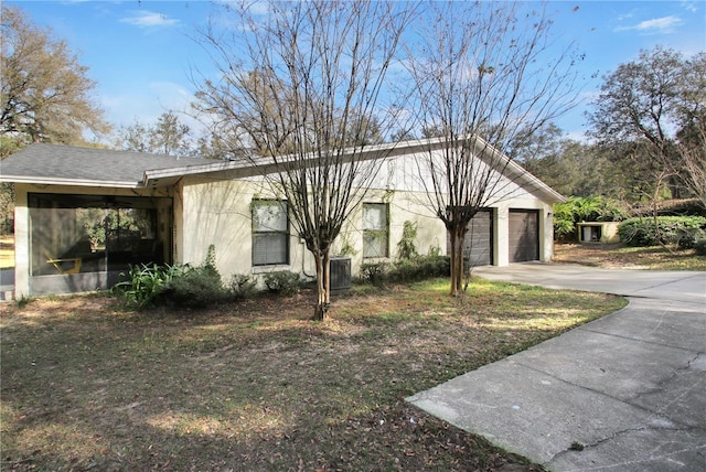 view of side of home featuring central air condition unit, a garage, concrete driveway, roof with shingles, and stucco siding