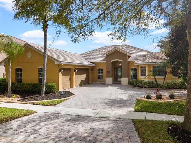 view of front of home with stucco siding, a tile roof, decorative driveway, and a garage