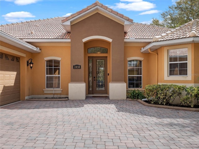 view of exterior entry featuring a tiled roof, stucco siding, and an attached garage