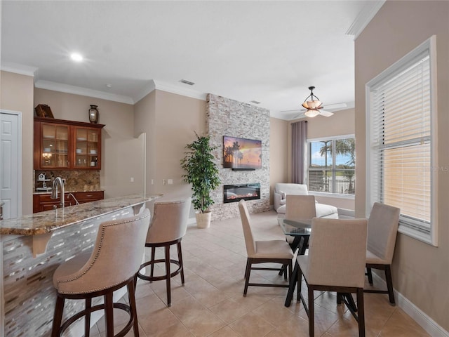 dining space featuring visible vents, crown molding, baseboards, light tile patterned floors, and a stone fireplace