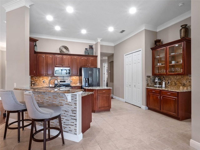 kitchen with a kitchen bar, light stone counters, stainless steel appliances, a peninsula, and glass insert cabinets