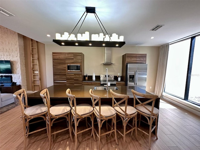 interior space featuring light wood-style floors, modern cabinets, a kitchen breakfast bar, stainless steel appliances, and wall chimney range hood