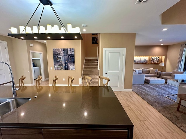 kitchen with light wood-style floors, a kitchen island with sink, open floor plan, and a sink