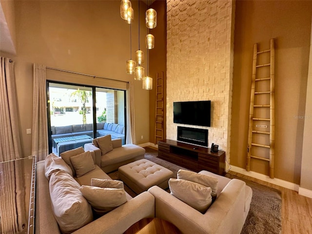 living room with a towering ceiling, baseboards, wood finished floors, and a stone fireplace