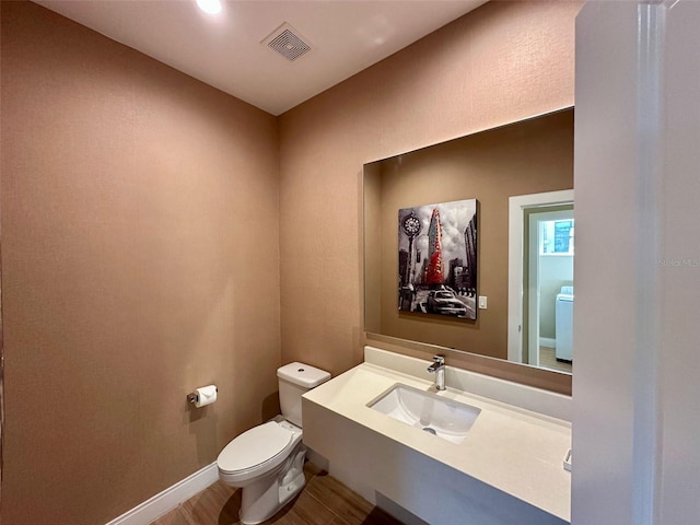 bathroom with washer / dryer, baseboards, visible vents, toilet, and wood finished floors