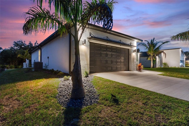 view of front of home with central AC unit, a garage, a yard, driveway, and stucco siding