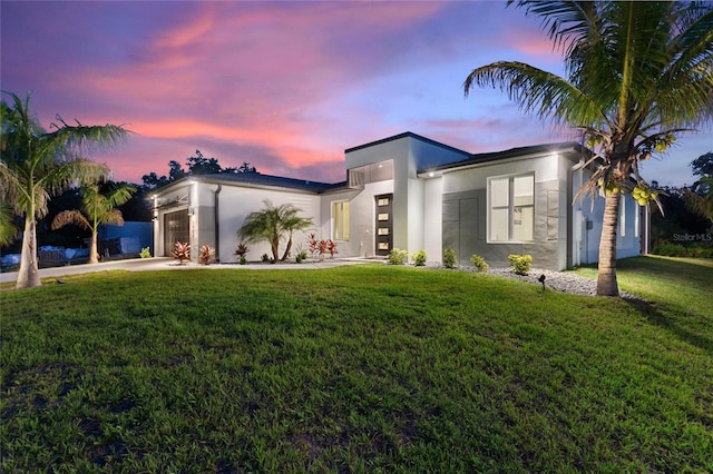 contemporary home with a garage, concrete driveway, a lawn, and stucco siding