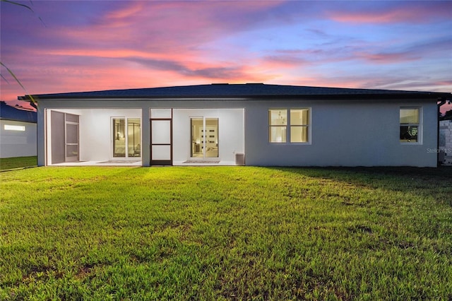 back of property featuring a lawn and stucco siding