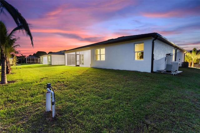 property exterior at dusk with a yard, central AC, and stucco siding