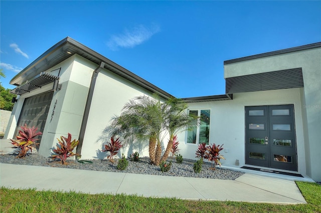 view of side of property with french doors, an attached garage, and stucco siding