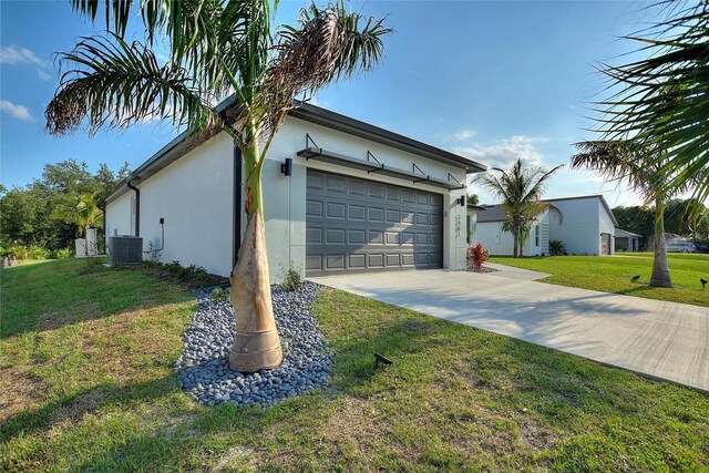 view of side of property featuring driveway, central AC unit, an attached garage, a yard, and stucco siding