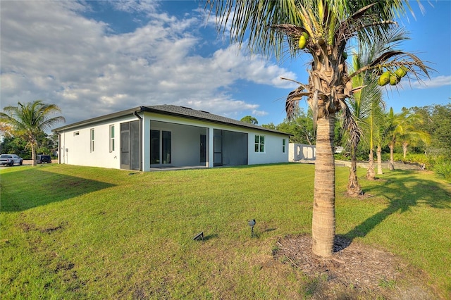 back of house featuring a sunroom, a lawn, and stucco siding