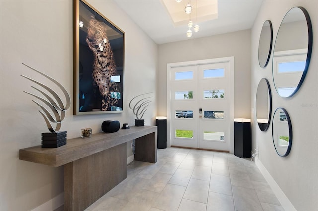 foyer entrance featuring a tray ceiling, french doors, baseboards, and light tile patterned floors