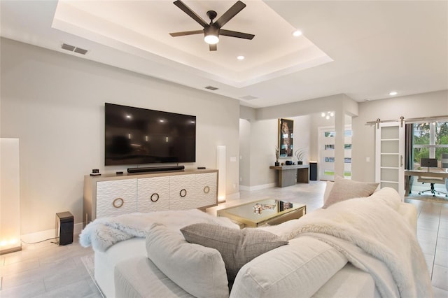 living room with a barn door, baseboards, visible vents, ceiling fan, and a tray ceiling