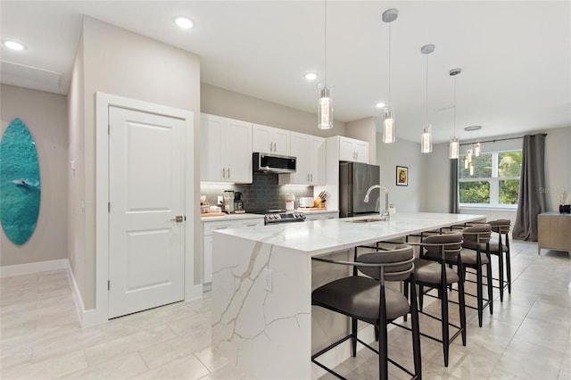 kitchen with white cabinets, decorative backsplash, a large island, stainless steel appliances, and a sink