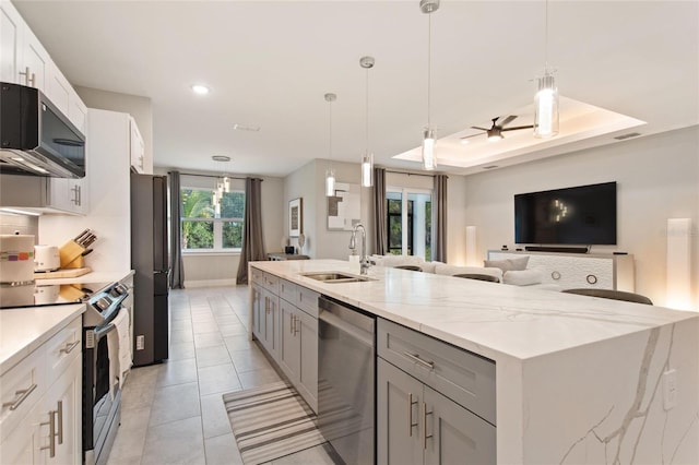 kitchen with a spacious island, appliances with stainless steel finishes, open floor plan, a tray ceiling, and a sink