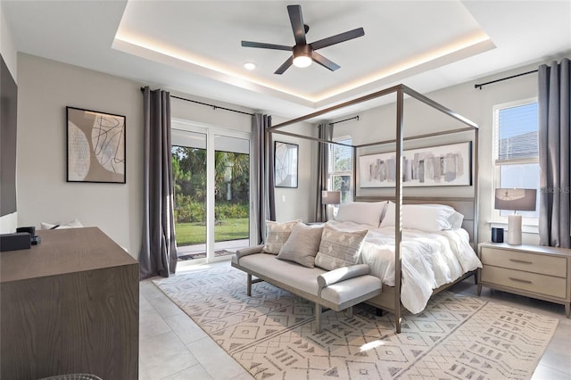 bedroom featuring access to exterior, multiple windows, a tray ceiling, and light tile patterned floors