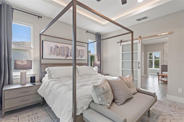 bedroom featuring light tile patterned floors, a barn door, visible vents, and baseboards