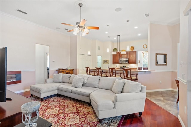 living room with visible vents, baseboards, ornamental molding, and light wood finished floors