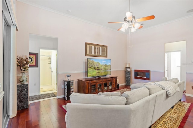 living area with a ceiling fan, a glass covered fireplace, dark wood finished floors, crown molding, and baseboards