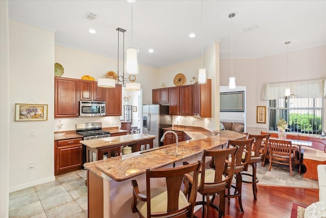 kitchen with light stone countertops, visible vents, a sink, appliances with stainless steel finishes, and a kitchen breakfast bar