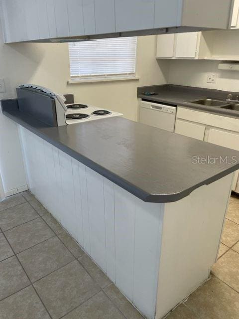 kitchen featuring dark countertops, light tile patterned floors, a peninsula, white dishwasher, and white cabinets