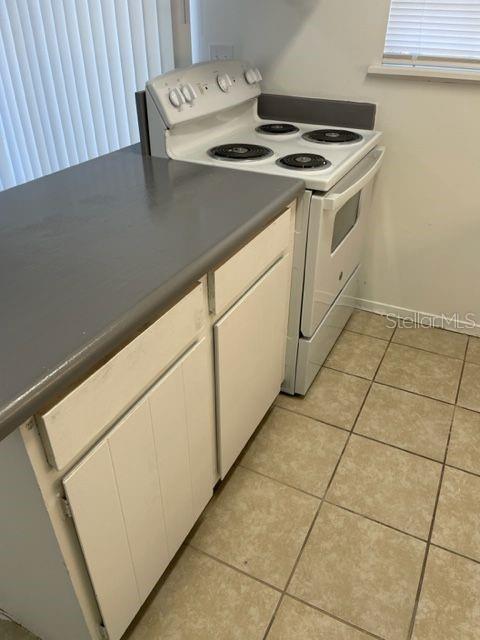 kitchen with electric stove, dark countertops, white cabinets, light tile patterned floors, and baseboards