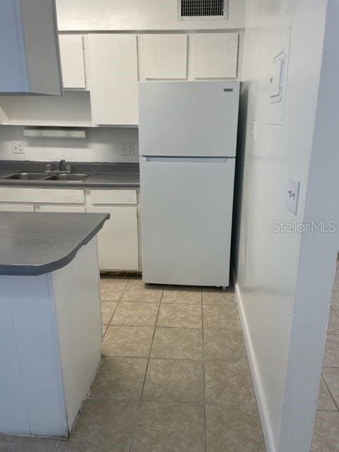 kitchen with dark countertops, visible vents, freestanding refrigerator, white cabinets, and a sink