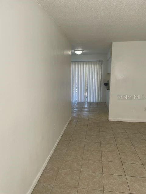 hallway featuring light tile patterned floors, a textured ceiling, and baseboards