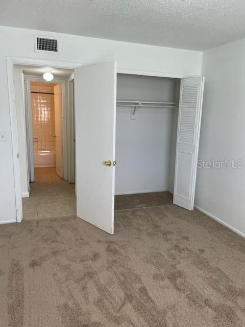 unfurnished bedroom featuring carpet flooring, visible vents, a closet, and a textured ceiling