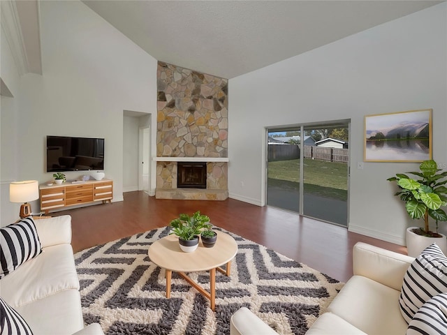 living room featuring high vaulted ceiling, a stone fireplace, wood finished floors, and baseboards