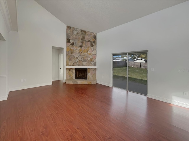 unfurnished living room featuring a textured ceiling, high vaulted ceiling, a fireplace, wood finished floors, and baseboards