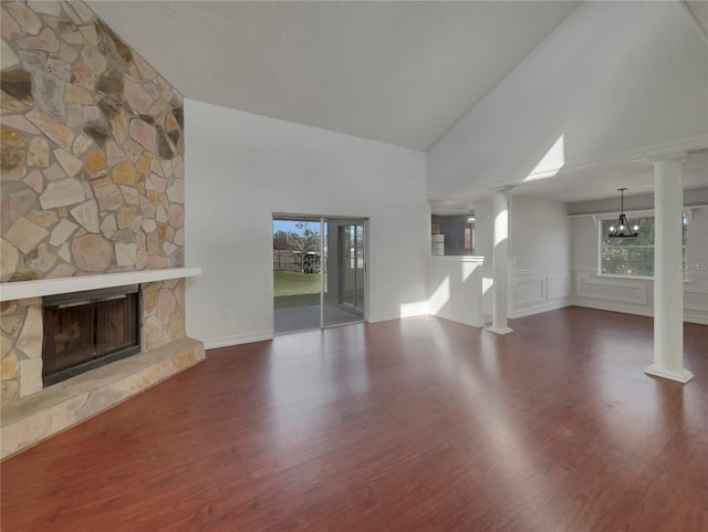 unfurnished living room featuring a chandelier, a fireplace, wood finished floors, and decorative columns