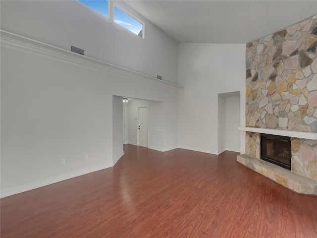 unfurnished living room with a textured ceiling, visible vents, wood finished floors, and a stone fireplace