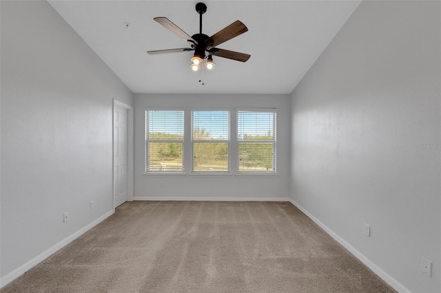 empty room featuring a ceiling fan, light colored carpet, vaulted ceiling, and baseboards