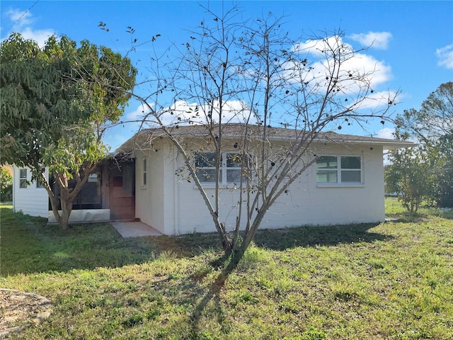 back of property with a sunroom, concrete block siding, and a yard