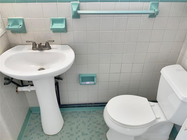 bathroom featuring toilet, a sink, and tile walls