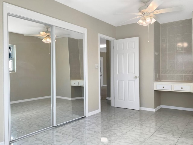 unfurnished bedroom featuring ceiling fan, marble finish floor, built in study area, and baseboards