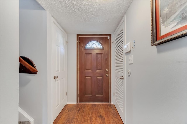 doorway to outside with a textured ceiling, baseboards, and wood finished floors