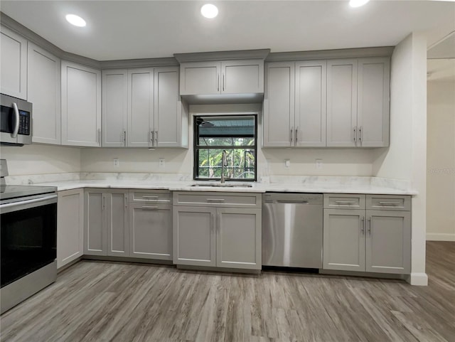 kitchen featuring light wood-type flooring, stainless steel appliances, a sink, and gray cabinetry