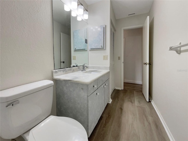 bathroom with visible vents, toilet, vanity, wood finished floors, and baseboards