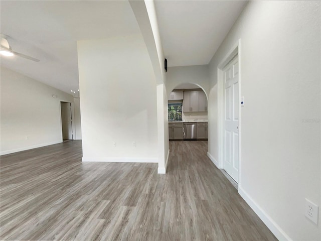 empty room with ceiling fan, arched walkways, wood finished floors, baseboards, and vaulted ceiling