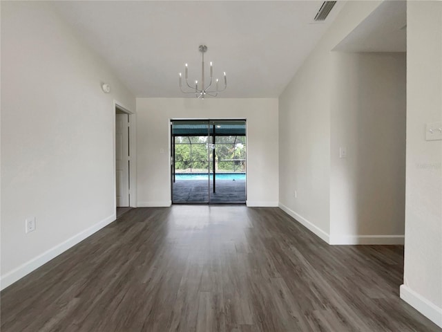 spare room featuring dark wood-style floors, baseboards, and an inviting chandelier