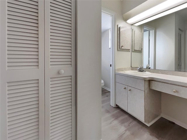 bathroom featuring baseboards, toilet, wood finished floors, vanity, and a closet