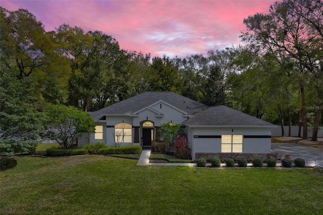 ranch-style house featuring an attached garage, a shingled roof, driveway, a lawn, and stucco siding